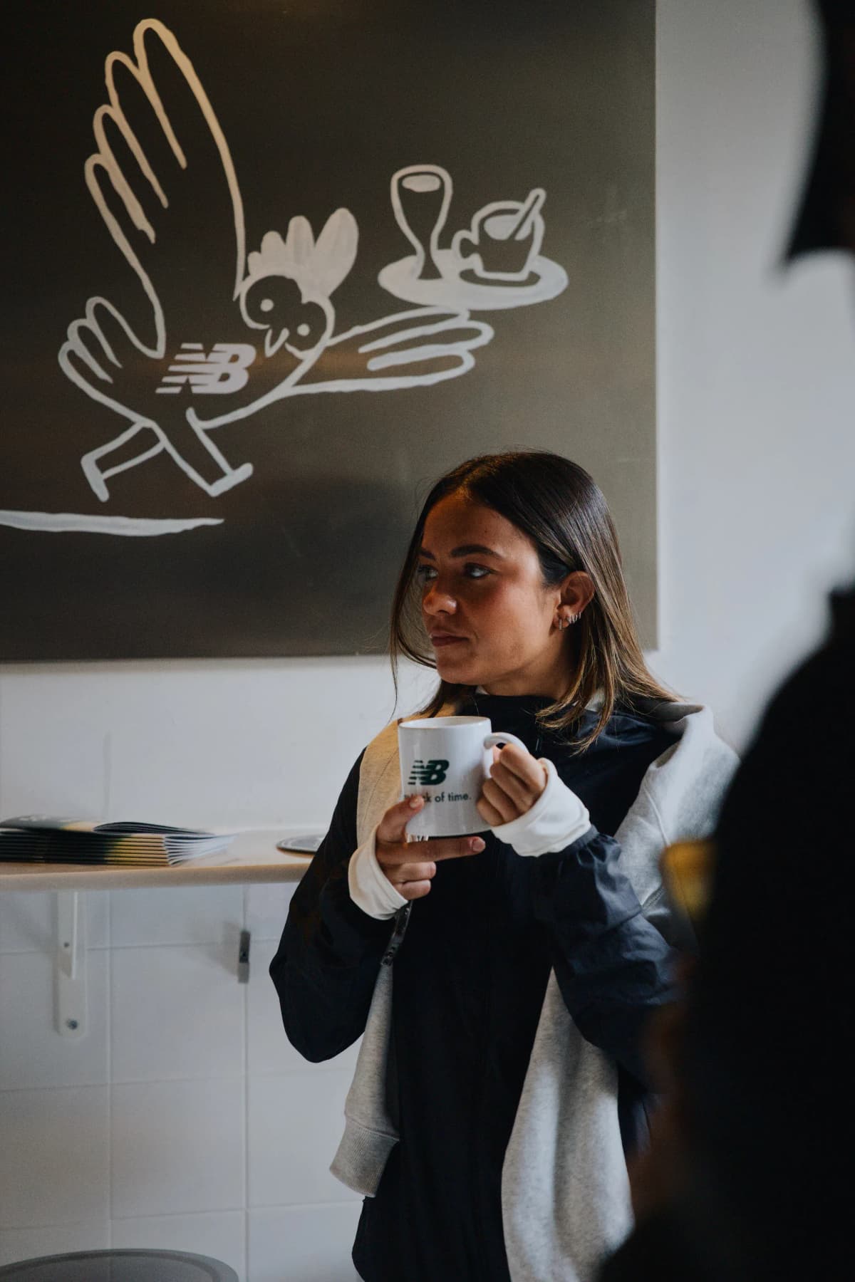 mujer tomando café con merch de newbalance